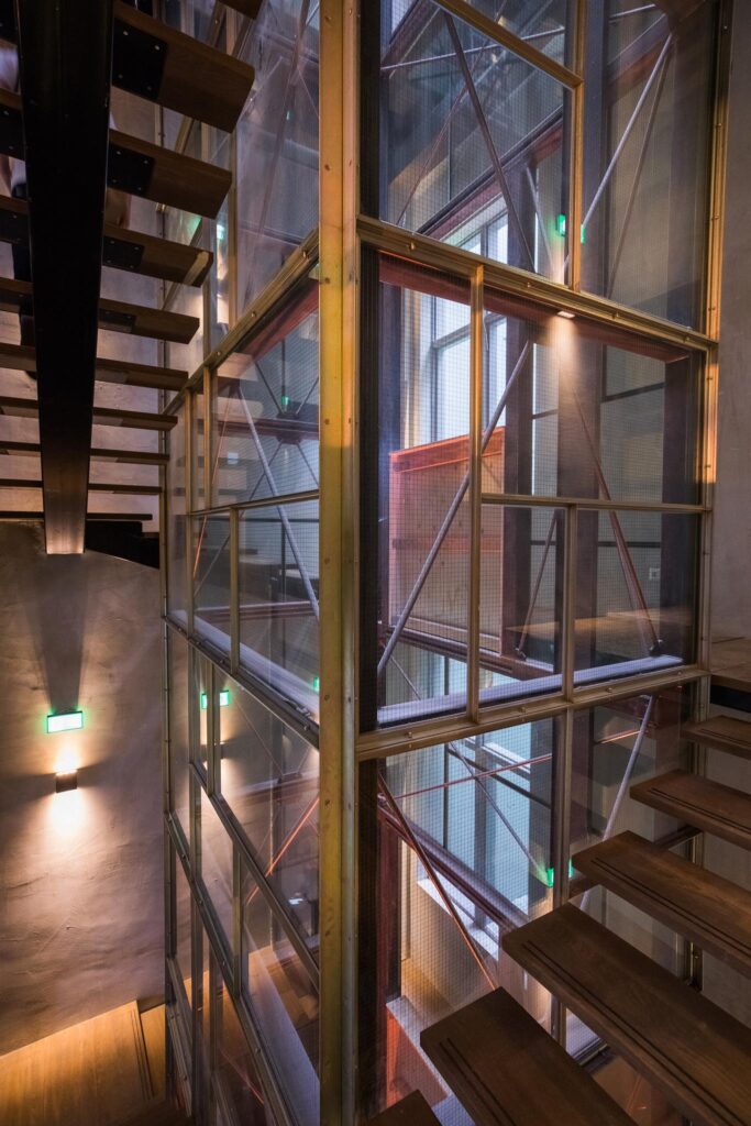 Moderne houten trap met industrieel ogende glazen liftconstructie aan de Prins Hendrikkade.